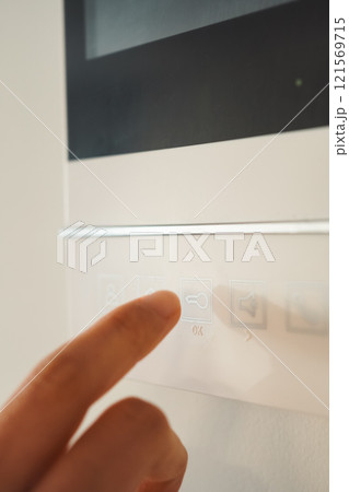 インターホン、電気錠連動のテレビドアホン 解錠のボタンを押そうとしている女性の手のクローズアップクロ インターホン、電気錠連動のテレビドアホン 解錠のボタンを押そうとしている女性の手のクローズアップクロ 121569715