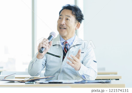 マイクを持って発言する作業服のミドルエイジの男性　撮影協力：学校法人電波学園 東京電子專門学校 121574131