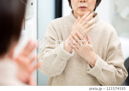 洗面所の鏡を見ながら手指のスキンケアをするミドル〜シニア女性 洗面所の鏡を見ながら手指のスキンケアをするミドル〜シニア女性 121574585