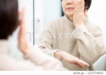 洗面所の鏡を見ながらスキンケアをするミドル〜シニア女性 121574603