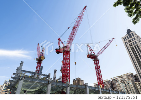 Low-angle view of cranes and steel structures of building construction with a blue sky background in Taiwan. Low-angle view of cranes and steel structures of building construction with a blue sky background in Taiwan. 121575551