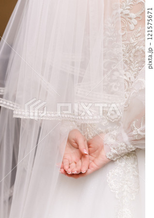 The bride in a wedding dress with a veil folded her hands behind her back 121575671