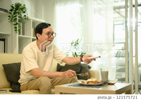 Smiling middle aged enjoying a meal and watching television in living room 121575721