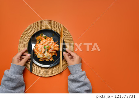 Above view of hands placing freshly homemade Kimchi on a woven mat against orange background 121575731