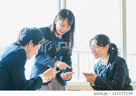 教室でクラスメイトとスマホを見ながら話す男女高校生 121577234
