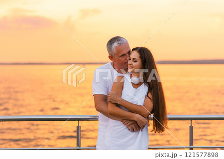 Happy couple is hugging on pier by the water. Young woman has long hair and the man is kissing her. Scene is romantic and peaceful 121577898