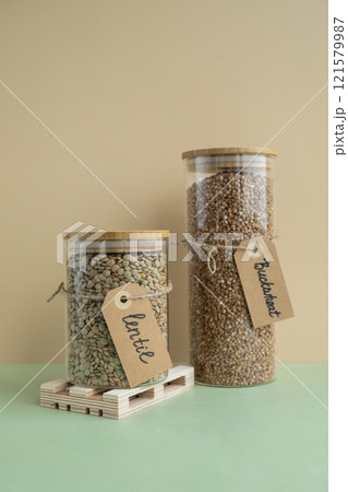 Refillable glass jar with raw buckwheat porridge and green lentil. Copy space Refill product format eco-friendly living. Filling reusable container Whole spelt grain species. High protein fiber-rich Refillable glass jar with raw buckwheat porridge and green lentil. Copy space Refill product format eco-friendly living. Filling reusable container Whole spelt grain species. High protein fiber-rich 121579987