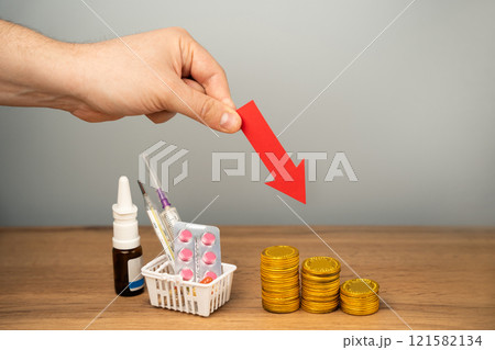 Down arrow, coins and basket with medical pills. Concept of reducing the price of medicines and drugs. Healthcare and medicine. Male hand 121582134