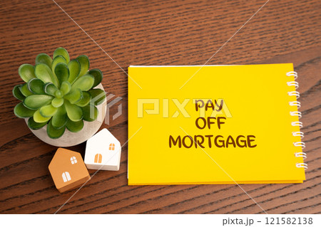 Pay off mortgage concept. Process of fully repaying the loan used to purchase a home. Notebook with inscription and miniature houses on the table. Real estate Pay off mortgage concept. Process of fully repaying the loan used to purchase a home. Notebook with inscription and miniature houses on the table. Real estate 121582138