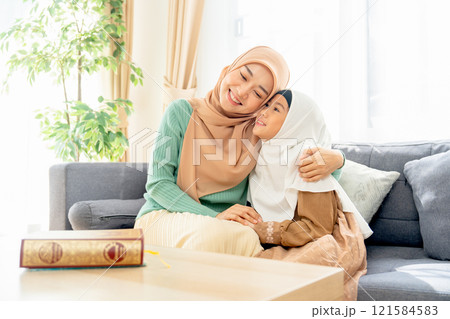 Asian muslim mother sit on sofa beside of her daughter and hug her child they also smiling in concept of happiness muslim family at home. Asian muslim mother sit on sofa beside of her daughter and hug her child they also smiling in concept of happiness muslim family at home. 121584583