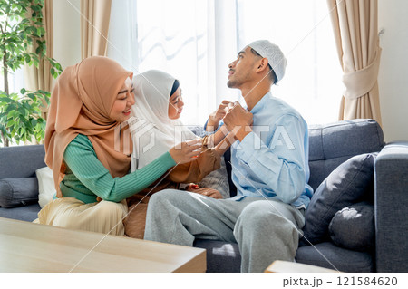 Little Asian muslim girl help her young father to wear shirt and stay together as family in living room of their house. 121584620