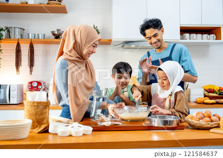 Asian muslim father, mother and brother cheer up the girl to mix flour in the bowl and stay together in kitchen of their house. 121584637
