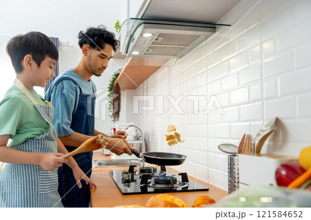 Young Asian father show skill of cooking by throwing pan cake up and his son cheer up beside in the kitchen of their house. Young Asian father show skill of cooking by throwing pan cake up and his son cheer up beside in the kitchen of their house. 121584652