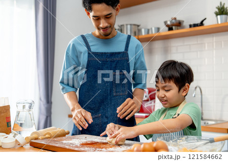 Asian father stand beside his son during teaching the boy to threshing flour for making bakery in kitchen of their house. Asian father stand beside his son during teaching the boy to threshing flour for making bakery in kitchen of their house. 121584662