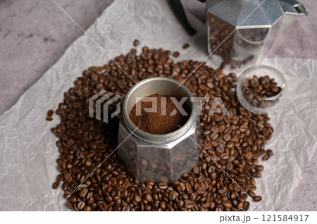 Ground coffee in a geyser coffee maker moka machine. Scattered fresh aromatic coffee beans around. Light background. Preparation to making coffee 121584917