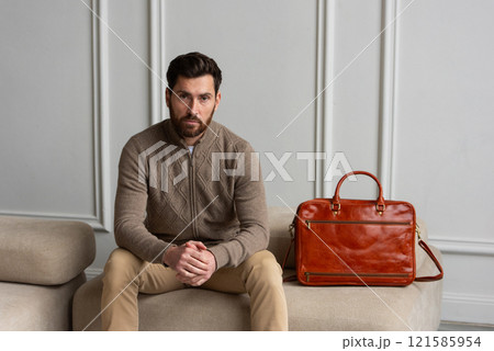 A man is comfortably sitting on a sofa, with a leather orange briefcase A man is comfortably sitting on a sofa, with a leather orange briefcase 121585954