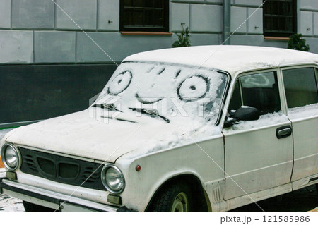 A funny car covered with snow, featuring a drawn smile and eyes on the windshield. 121585986