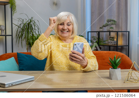 Senior grandmother woman at home use smartphone celebrating success victory winning play online game 121586064