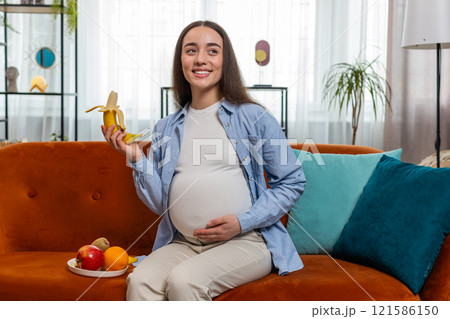 Happy pregnant woman with great appetite peels and eats banana fruit at home healthy food concept Happy pregnant woman with great appetite peels and eats banana fruit at home healthy food concept 121586150