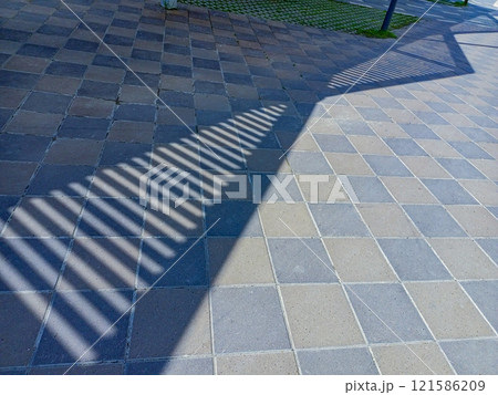 Paving slabs laid out on a pedestrian walking park, on which a shadow falls, with strips of light decreasing in length, creating an abstract arrow pointing to the correct direction of movement. 121586209