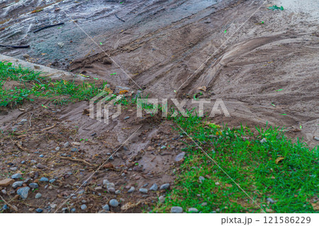 Traces of mud flows of earth washed away from green areas of park to the surface of asphalt in the process of sudden flooding with huge amount of water due to a downpour or burst water pipe 121586229