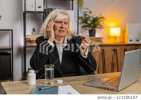 Sick senior businesswoman suffering from headache taking medicine and working on laptop at home Sick senior businesswoman suffering from headache taking medicine and working on laptop at home 121586287