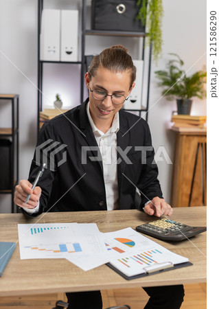 Successful businessman analyzing financial report while using calculator sitting at home office desk Successful businessman analyzing financial report while using calculator sitting at home office desk 121586290