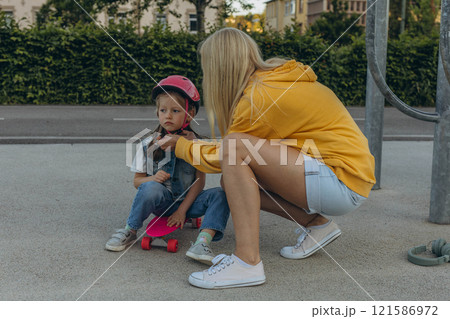 Mom helping her daughter to put on a helmet and ride a skateboard 121586972