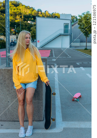 a young blonde girl in a yellow sweatshirt rides on the skateboard in the skate park 121586975