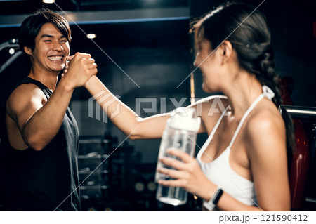 Asian woman and man working out together in gym interior and holding hands, smile couple holding hold hand after complete training at fitness gym, sport workout healthy lifestyle concept 121590412