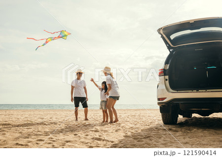 Asian family is flying a kite while running on the beach. Happy parents mother and father with their child playing with kite, The car is parked nearby, and the family is enjoying their time together 121590414