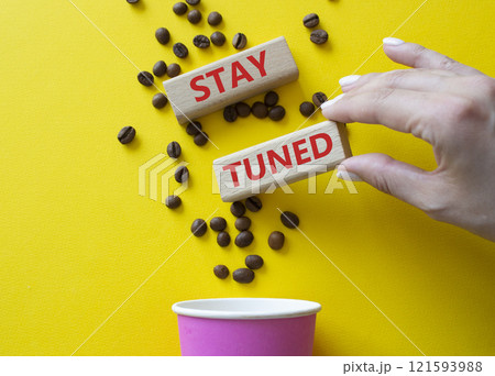 Stay Tuned symbol. Concept word Stay Tuned on wooden blocks. Businessman hand. Beautiful yellow background with coffee cup. Business and Stay Tuned concept. Copy space 121593988