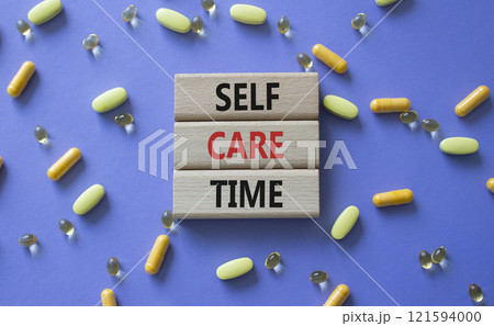 Self-care Time symbol. Concept words Self-care Time on wooden blocks. Beautiful purple background with pills. Healthcare and Self-care Time concept. Copy space. 121594000