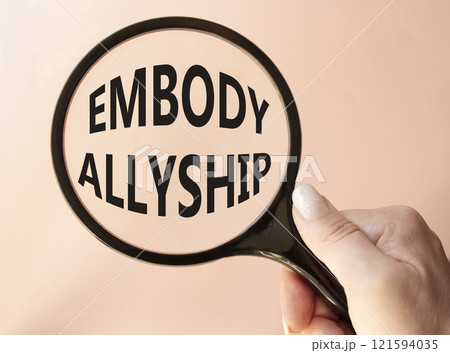 Embody Allyship symbol. Concept word Embody Allyship on magnifying glass. Beautiful pink background. Businessman hand. Business and Embody Allyship concept. Copy space 121594035