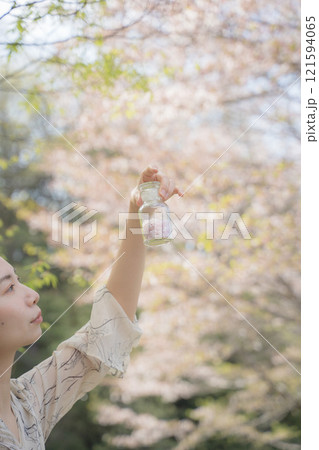 桜の下で桜の花びらの瓶を持つ女性 121594065
