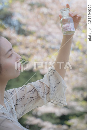 桜の下で桜の花びらの瓶を持つ女性 121594090