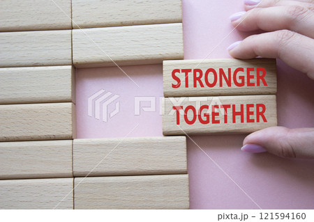 Stronger together symbol. Wooden blocks with words Stronger together. Businessman hand. Beautiful pink background. Stronger together concept. Copy space. Stronger together symbol. Wooden blocks with words Stronger together. Businessman hand. Beautiful pink background. Stronger together concept. Copy space. 121594160