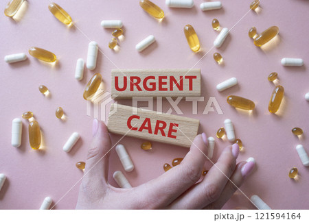 Urgent Care symbol. Concept word Urgent Care on wooden blocks. Beautiful pink background with pills. Doctor Hand. Medicine and Urgent Care concept. Copy space 121594164