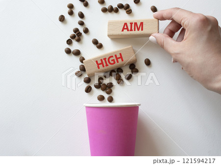 Aim High symbol. Concept word Aim High on wooden blocks. Beautiful white background with coffee cup. Businessman hand. Business and Aim High concept. Copy space 121594217