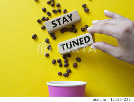 Stay Tuned symbol. Concept word Stay Tuned on wooden blocks. Businessman hand. Beautiful yellow background with coffee cup. Business and Stay Tuned concept. Copy space 121594222