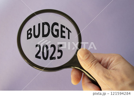 Budget 2025 symbol. Magnifying Glass with words Budget 2024. Beautiful purple background. Businessman hand. Business and Budget 2025 concept. Copy space. 121594284