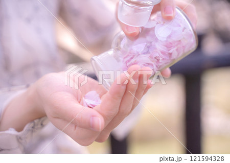桜の花びらを閉じ込めた瓶を手に持つ女性の手元 桜の花びらを閉じ込めた瓶を手に持つ女性の手元 121594328