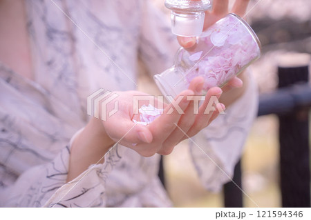 桜の花びらを閉じ込めた瓶を手に持つ女性の手元 121594346