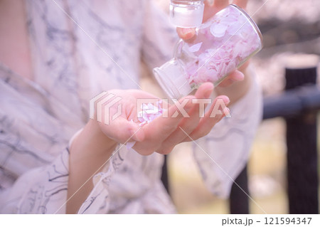 桜の花びらを閉じ込めた瓶を手に持つ女性の手元 121594347