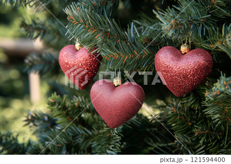 Close-up of red heart-shaped ornaments on a Christmas tree with festive lights. Christmas balls in a shape of a heart. Love and romantic symbol, Saint Valentine's Day background 121594400