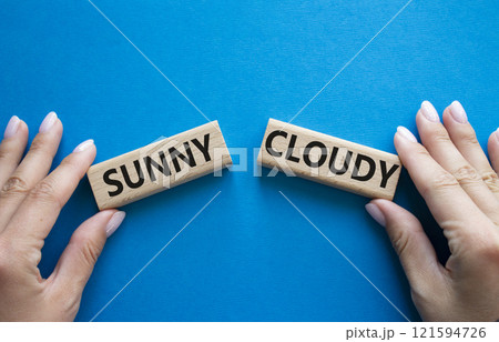 Sunny or Cloudy symbol. Concept word Sunny or Cloudy on wooden blocks. Businessman hand. Beautiful blue background. Business and Sunny or Cloudy concept. Copy space Sunny or Cloudy symbol. Concept word Sunny or Cloudy on wooden blocks. Businessman hand. Beautiful blue background. Business and Sunny or Cloudy concept. Copy space 121594726
