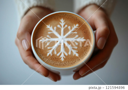 Hands in white sweater cuffs holding a cup of coffee or cocoa with a snowflake latte art on its foam, evoking winter themes, comfort, and coziness during cold seasons. Coffee lovers concept 121594896