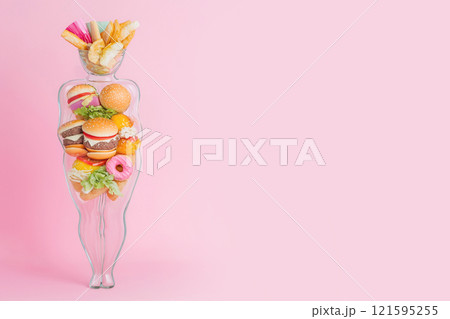 Female figure made out of unhealthy fast food. Glass vase full of junk food forming an obese figure as a symbol of unhealthy eating, wrong food choices. Overweight human silhouette, diet concept 121595255