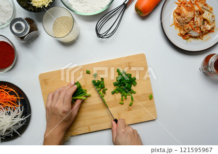 Hands chopping green onions on wooden cutting board surrounded by essential ingredients for making traditional Kimchi Hands chopping green onions on wooden cutting board surrounded by essential ingredients for making traditional Kimchi 121595967