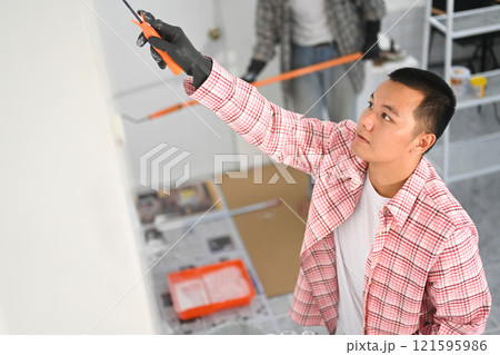 Young asian man painting a wall with a roller brush during a home renovation project Young asian man painting a wall with a roller brush during a home renovation project 121595986